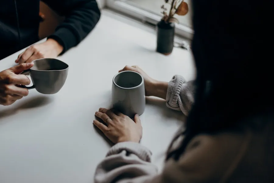 Ilustrasi mimpi bertemu mantan — two people holding gray mugs at table