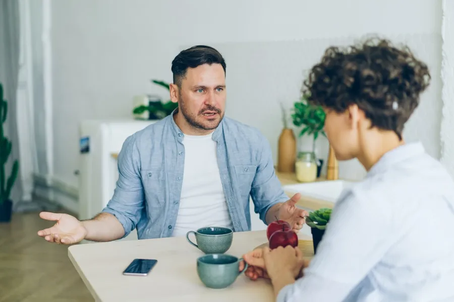 Ilustrasi mimpi bertengkar — a man sitting at a table talking to a woman
