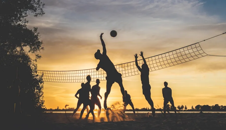 Ilustrasi mimpi bola voli — silhouettes playing beach volleyball at sunset