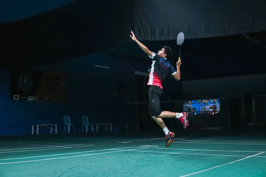 Ilustrasi mimpi bulu tangkis — man in white and red crew neck t-shirt and black shorts playing basketball
