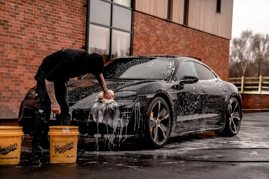 Ilustrasi mimpi cuci mobil — man in black t-shirt and black pants doing water splash on black coupe during daytime
