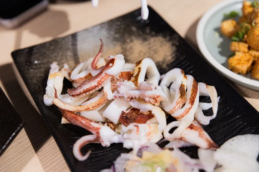 Ilustrasi mimpi cumi-cumi — Cooked squid tentacles and rings on a black plate.