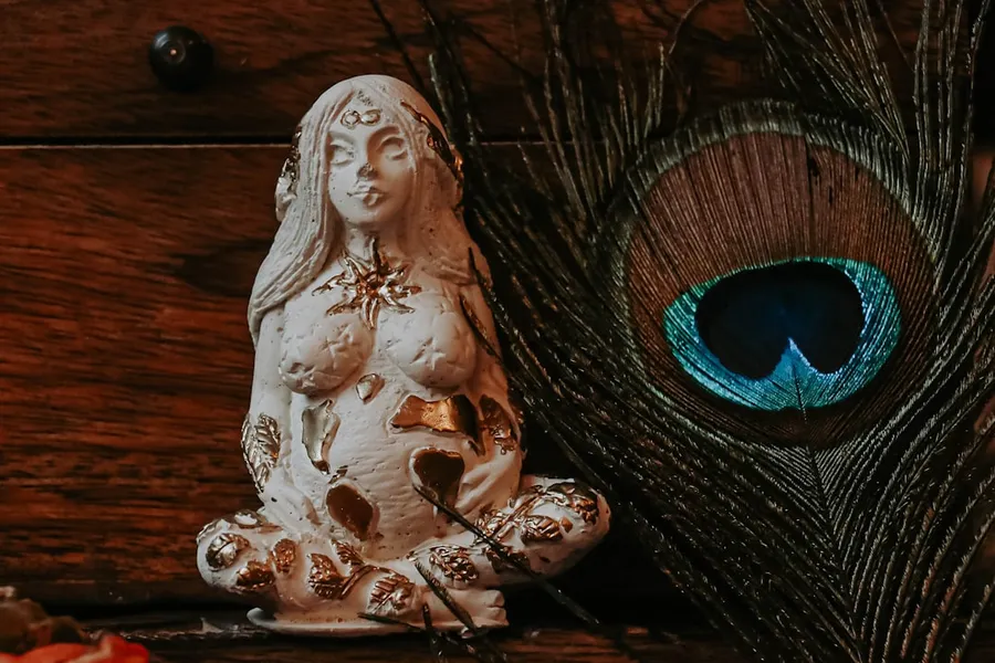 Ilustrasi mimpi dewi bulan — a statue of a woman sitting next to a peacock feather