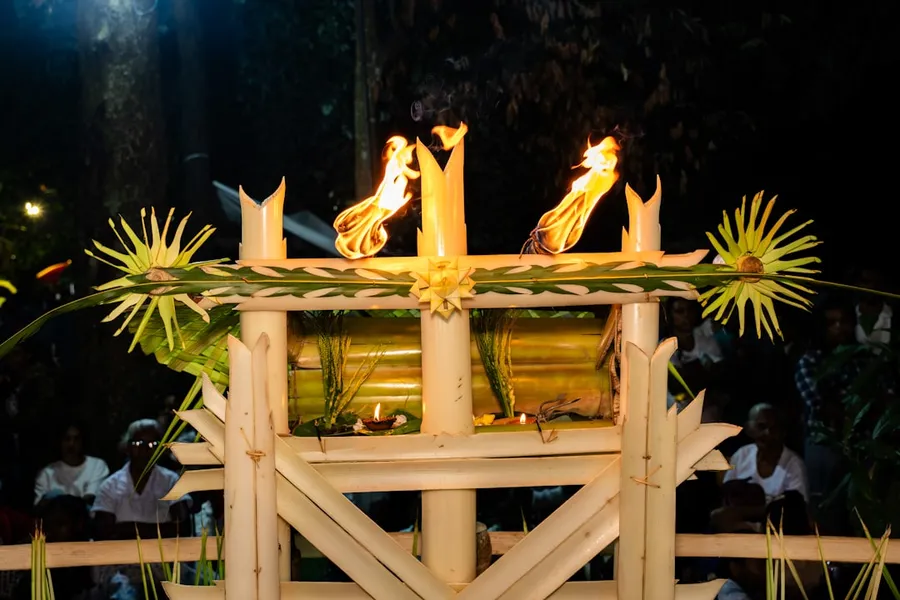 Ilustrasi mimpi dewi supraba — Three candles burn atop a decorated wooden structure at night.