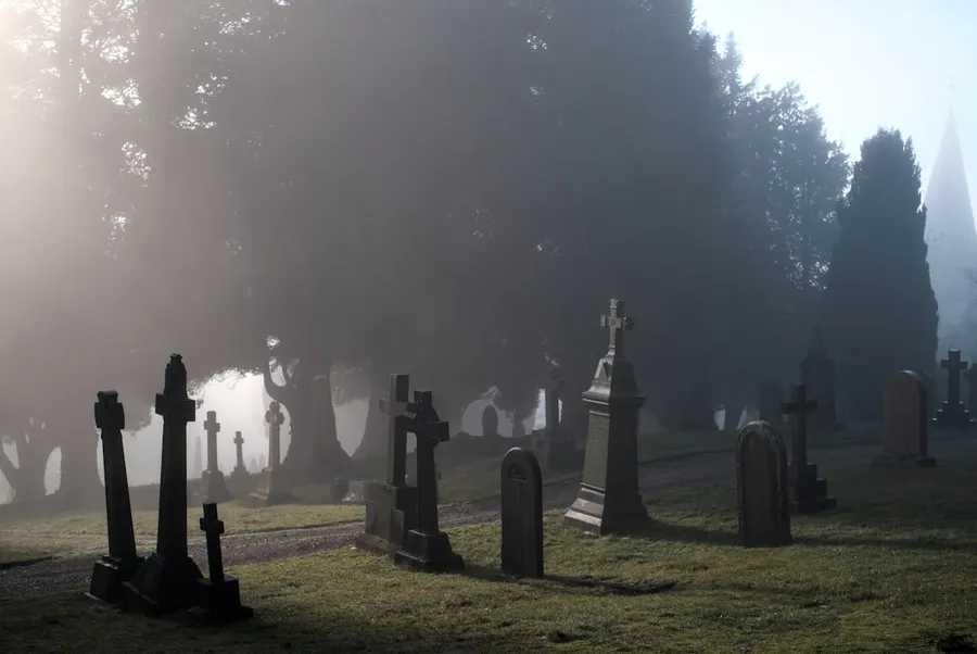 Ilustrasi mimpi hantu pocong — a foggy graveyard with tombstones in the foreground