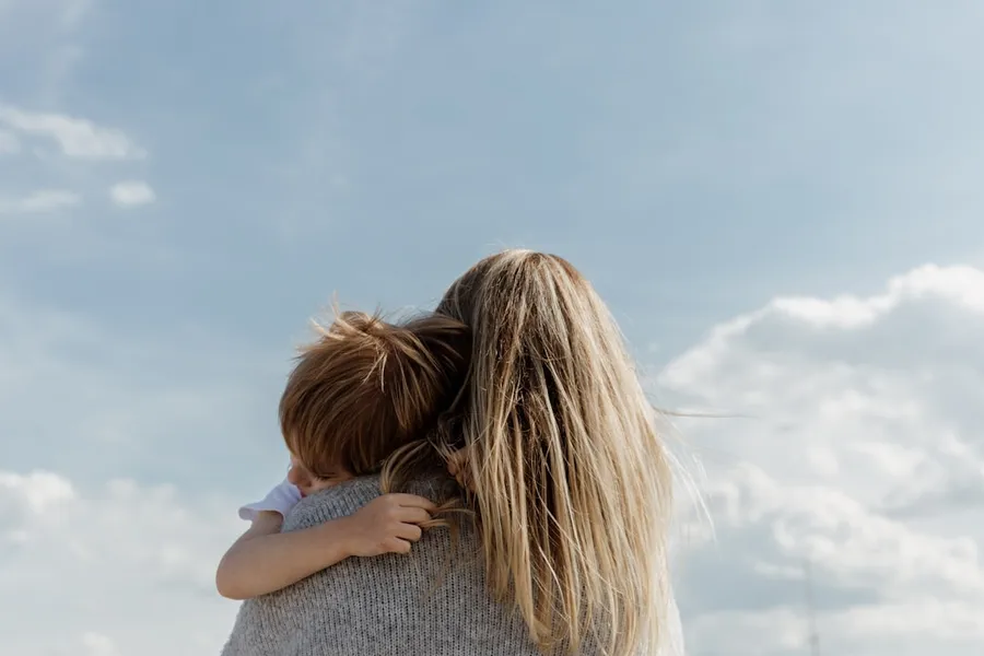 Ilustrasi mimpi ibu angkat — woman holding child from behind against cloudy sky