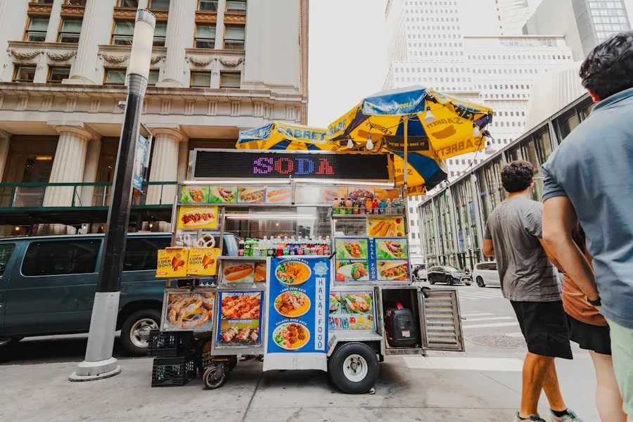 Ilustrasi mimpi jual bakso — A man and a woman standing next to a food cart