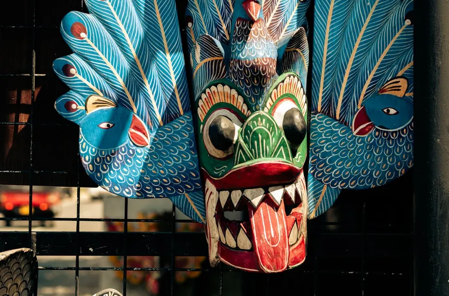 Ilustrasi mimpi kangsa dewa — A colorful wooden mask with peacock feathers