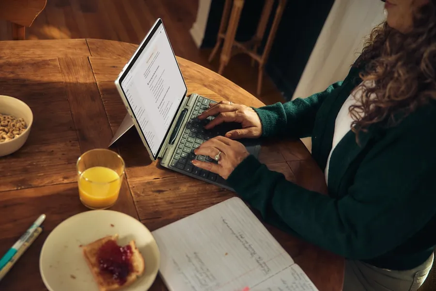 Ilustrasi mimpi kantor pemerintah — Woman typing on laptop at wooden table with breakfast.