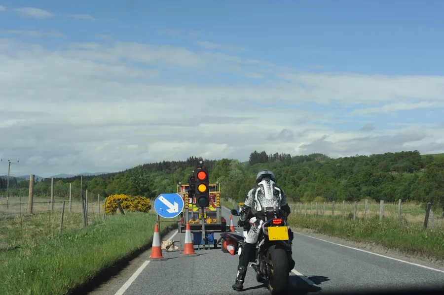 Ilustrasi mimpi kecelakaan motor — Motorcyclist stopped at red temporary traffic light on rural road.