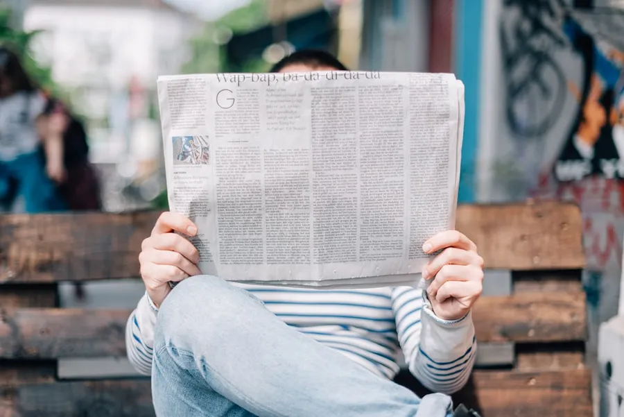 Ilustrasi mimpi koran — man sitting on bench reading newspaper
