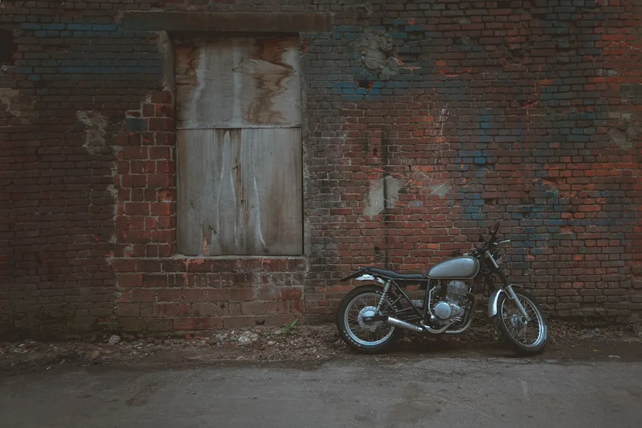 Ilustrasi mimpi kuda besi — black motorcycle parked beside brown brick wall