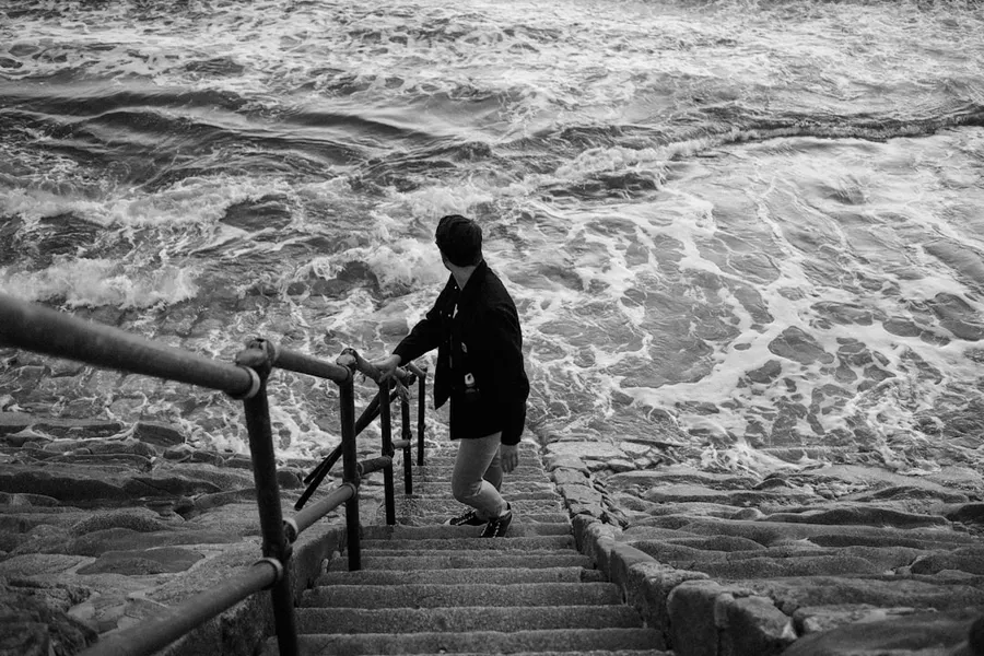 Ilustrasi mimpi laut pasang — man in black jacket walking on wooden bridge