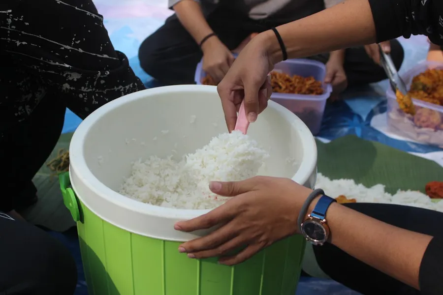 Ilustrasi mimpi makan nasi — a group of people sitting around a bucket of rice