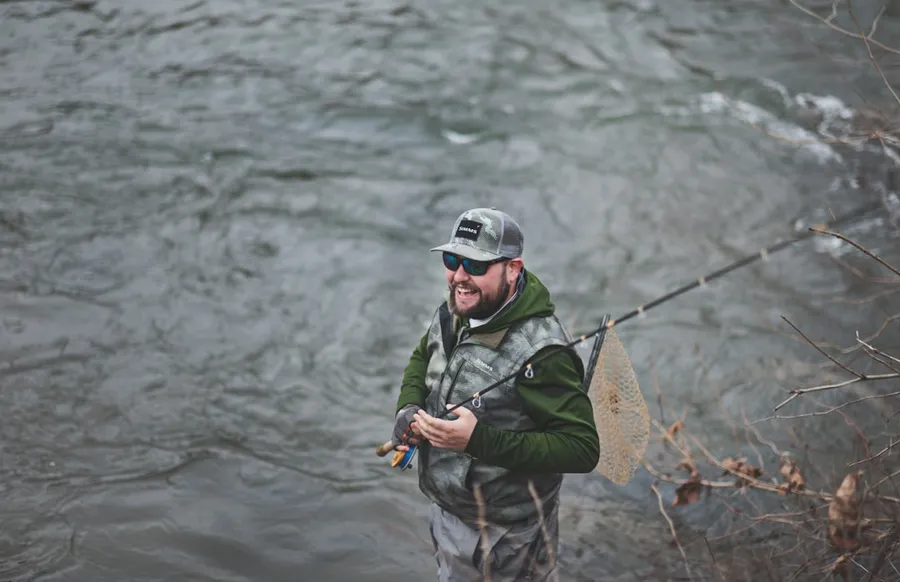 Ilustrasi mimpi mancing — man smiling holding black fishing rod near body of water