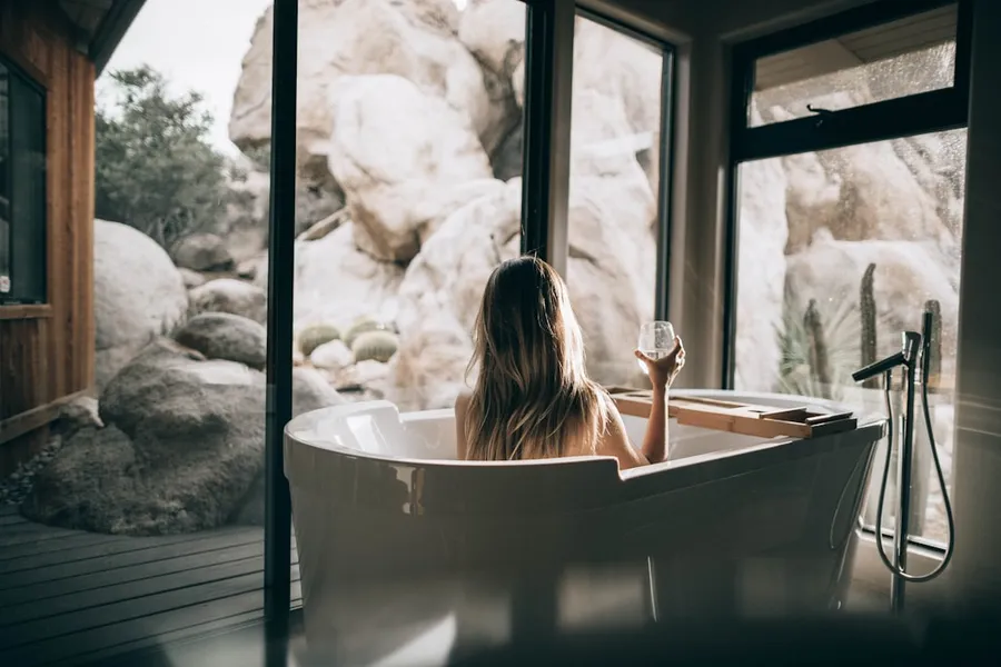 Ilustrasi mimpi mandi — woman in white bathtub holding clear drinking glass