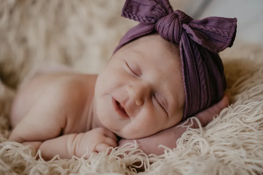 Ilustrasi mimpi melahirkan bayi perempuan — baby in purple knit cap lying on white fur textile