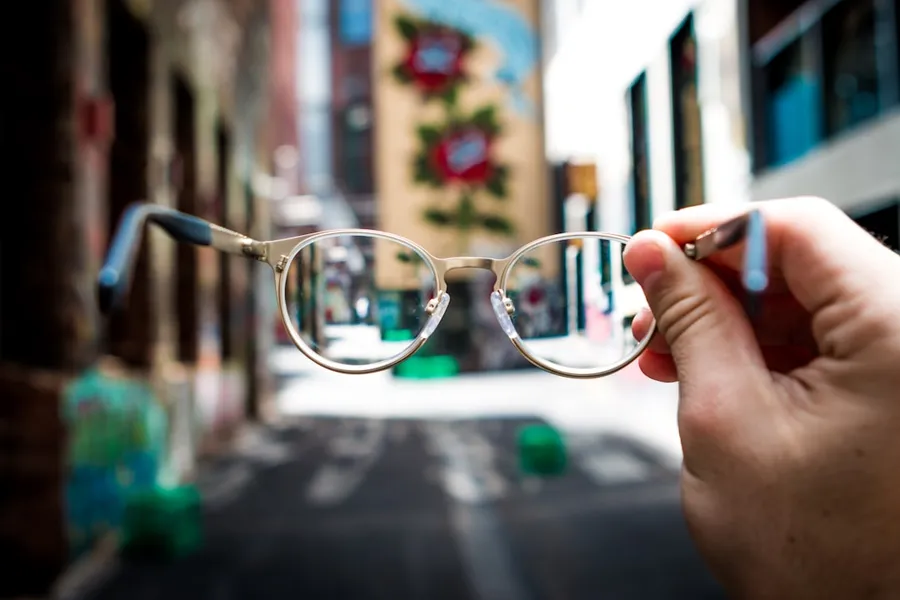 Ilustrasi mimpi memakai kacamata — person holding eyeglasses