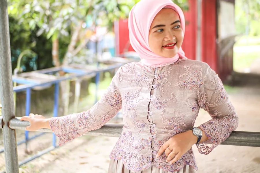 Ilustrasi mimpi memakai kebaya — A woman wearing a hijab smiles outdoors.