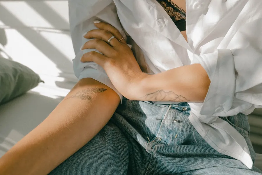 Ilustrasi mimpi memar — woman in white button up shirt and blue denim shorts sitting on white textile