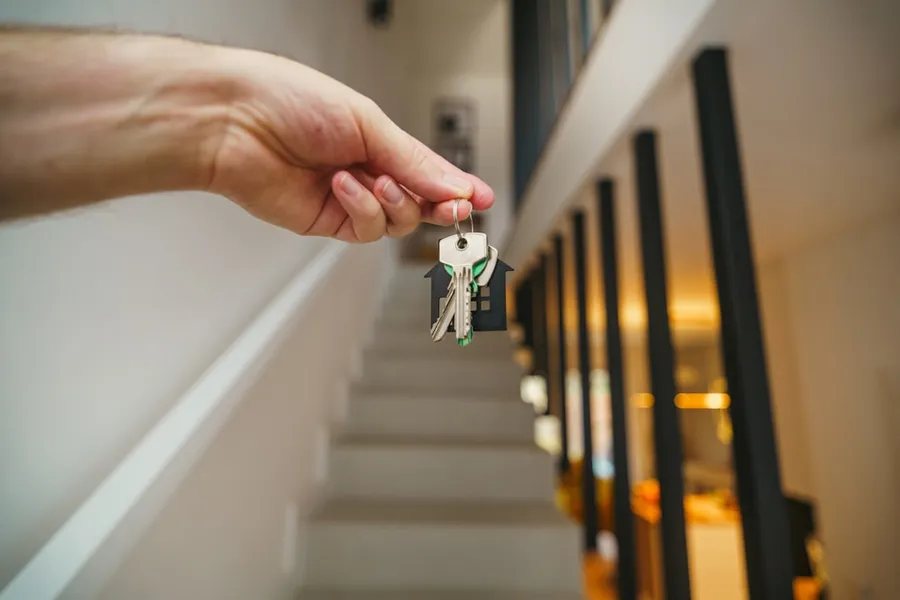 Ilustrasi mimpi membeli rumah — Here's a possible caption: keys being held in front of a staircase.