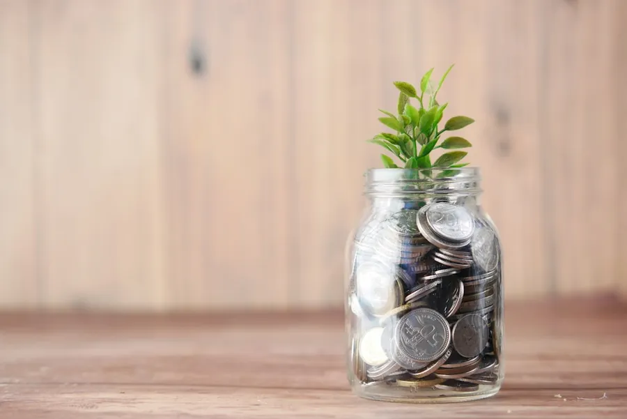 Ilustrasi mimpi menabung uang — a glass jar filled with coins and a plant