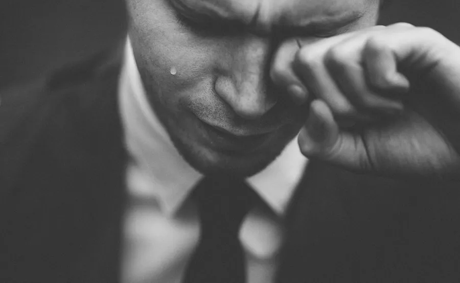 Ilustrasi mimpi menangis — man wiping his tears
