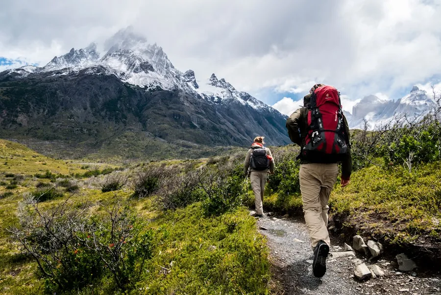 Ilustrasi mimpi mendaki gunung — two person walking towards mountain covered with snow