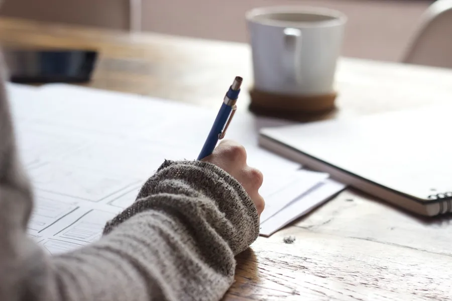 Ilustrasi mimpi menulis — person writing on brown wooden table near white ceramic mug