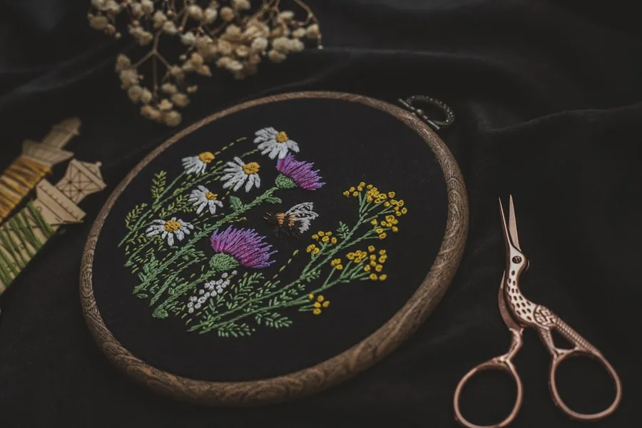 Ilustrasi mimpi menyulam — a close up of a embroidery on a black cloth with a pair of scissors