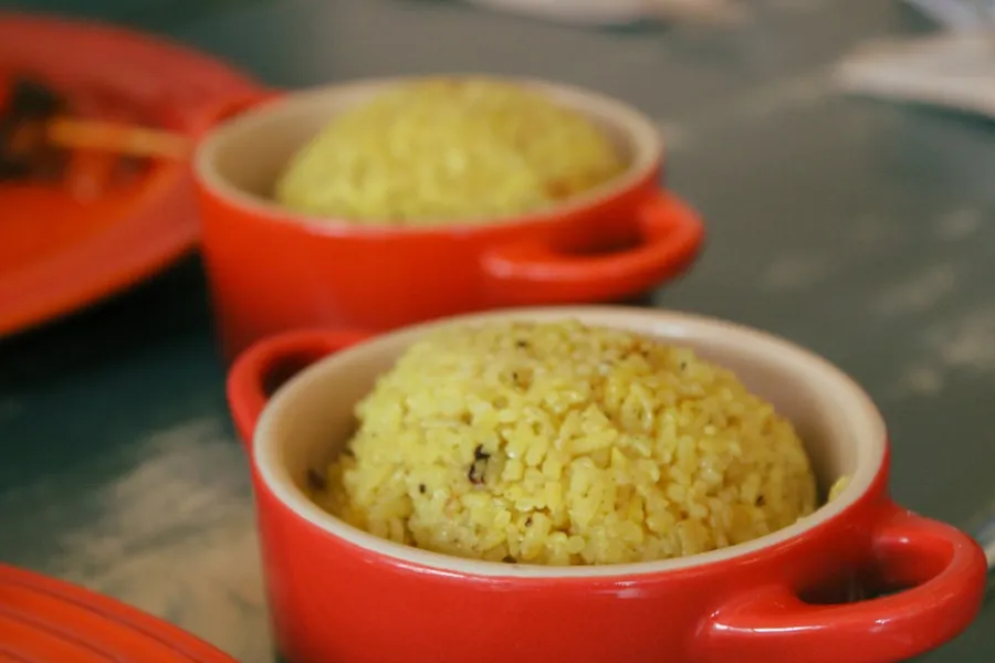Ilustrasi mimpi nasi kuning — Two red ramekins filled with yellow rice on a table.