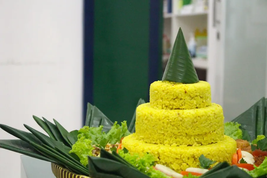 Ilustrasi mimpi nasi tumpeng — A three-tiered rice cake with green leaves.