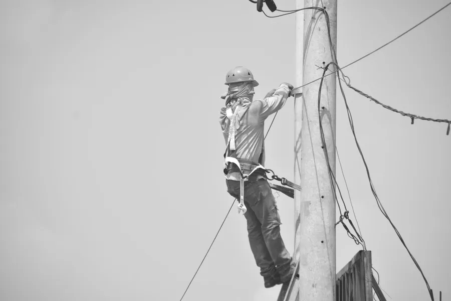 Ilustrasi mimpi panjat pinang — Lineman working on a utility pole with safety harness.