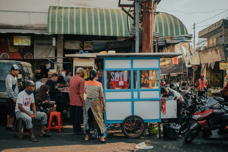 Ilustrasi mimpi pedagang kaki lima — people standing near blue and white food stall during daytime