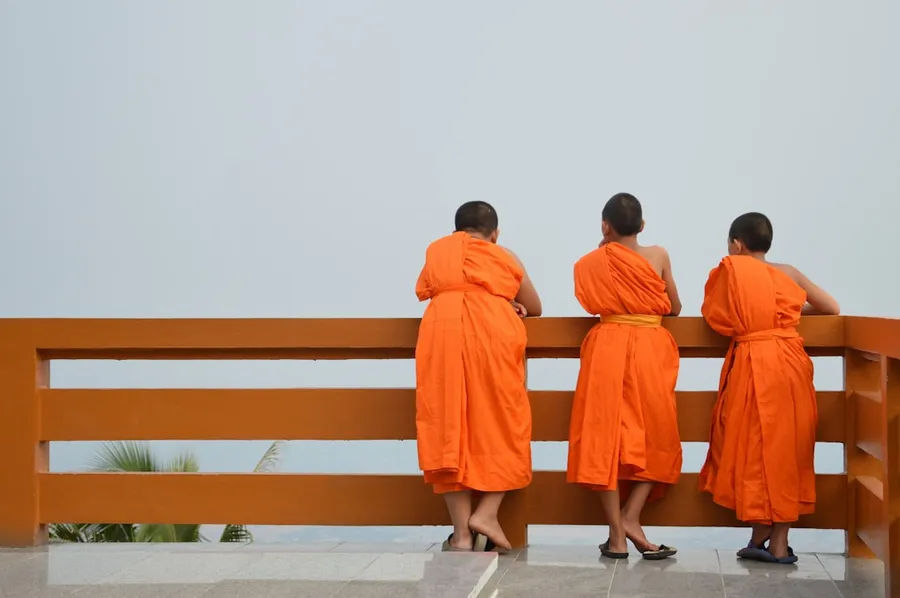 Ilustrasi mimpi pendeta sakti — three people in orange robes standing on a bench