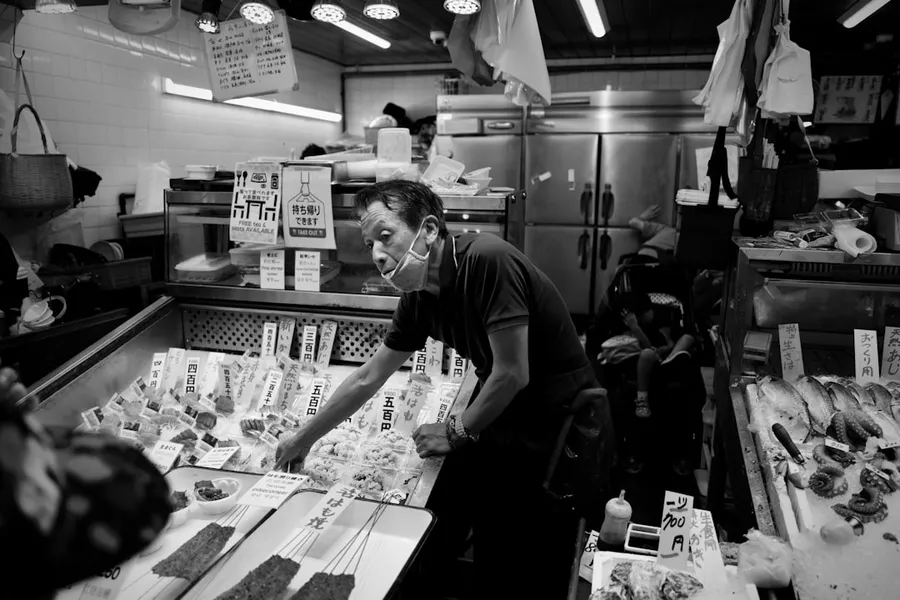 Ilustrasi mimpi penjaga toko — grayscale photo of man in crew neck t-shirt standing in front of store