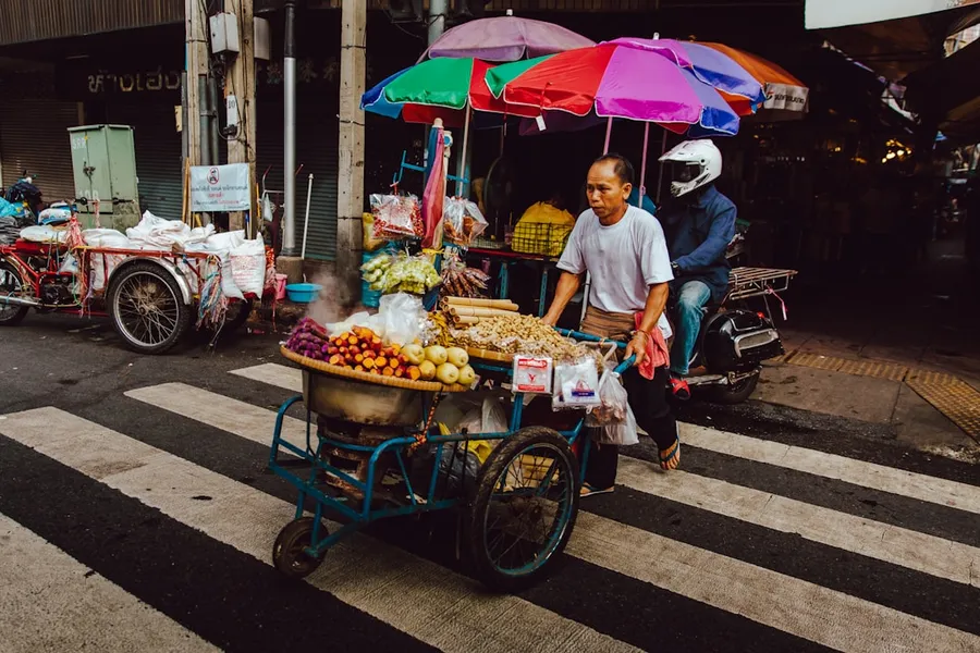 Ilustrasi mimpi penjual buah — man pushing his food cart on pedestrian lane during daytime