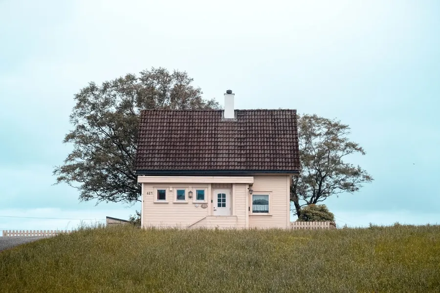 Ilustrasi mimpi pindah rumah — white and black concrete house near green trees under white sky during daytime