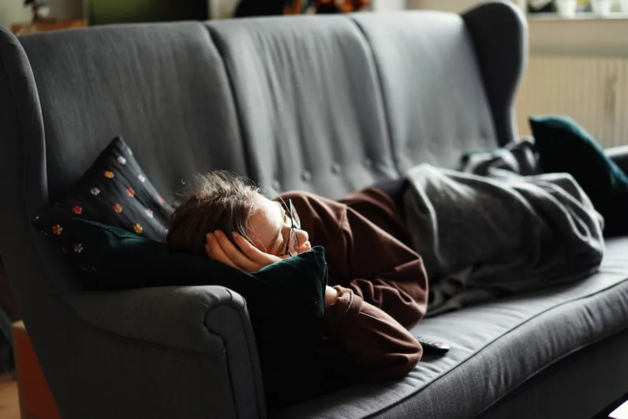 Ilustrasi mimpi pingsan — woman in pink jacket lying on gray couch
