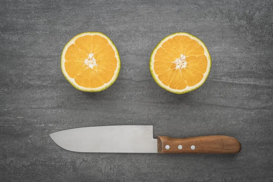 Ilustrasi mimpi pisau buah — sliced orange fruit beside black handled knife