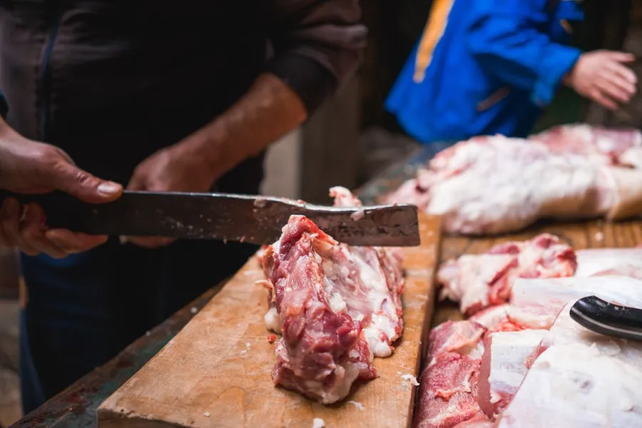 Ilustrasi mimpi potong babi — person chopping meat on board