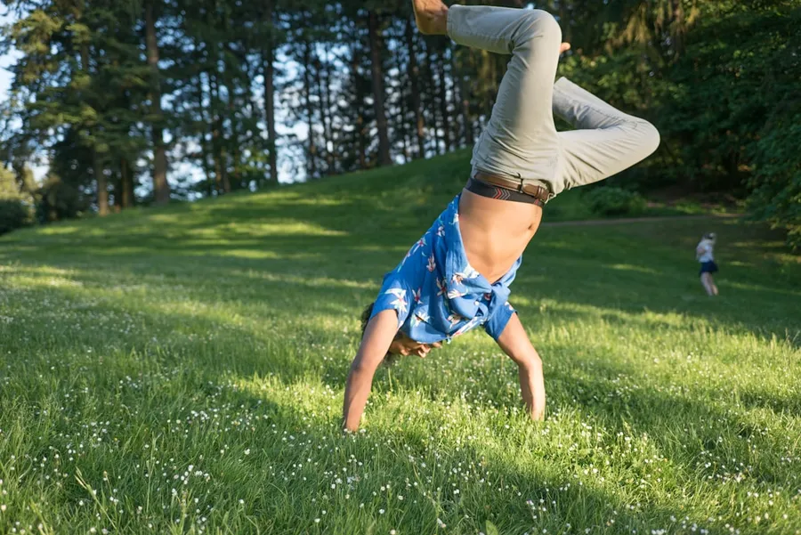 Ilustrasi mimpi salto — man in blue shirt and jeans standing upside down in grass field