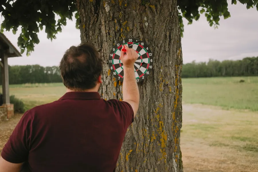 Ilustrasi mimpi sawatan — Man throwing dart at a tree-mounted dartboard.