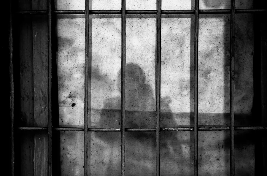 Ilustrasi mimpi tawanan — a shadow of a person behind bars in a jail cell