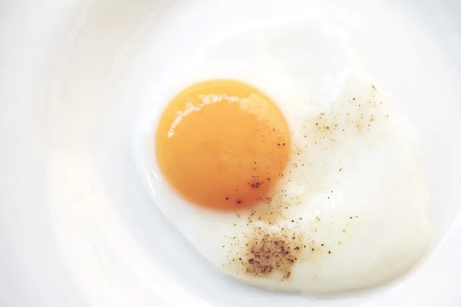 Ilustrasi mimpi telur ceplok — sunny side up egg on white ceramic plate