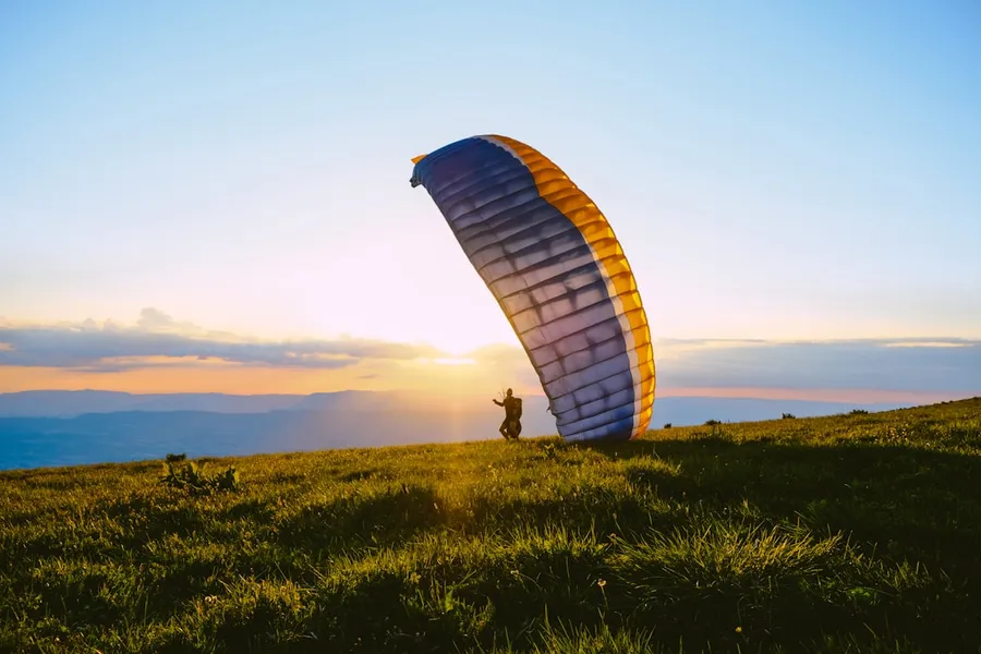 Ilustrasi mimpi terbang layang — silhouette of person riding parachute during sunset