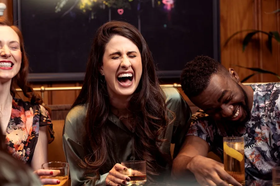 Ilustrasi mimpi tertawa lepas — a group of people sitting around a table with drinks