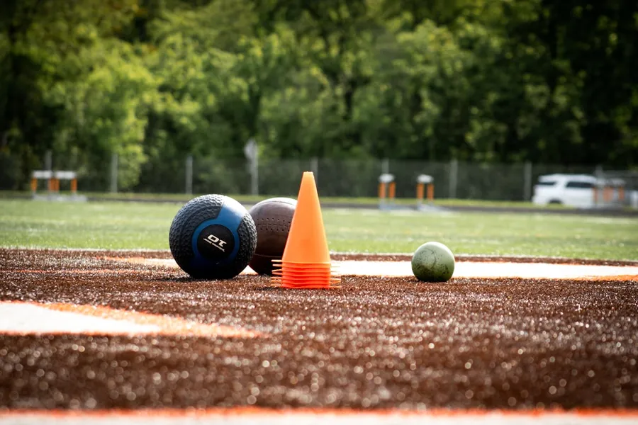 Ilustrasi mimpi tolak peluru — Medicine balls and an orange cone on a dirt track.