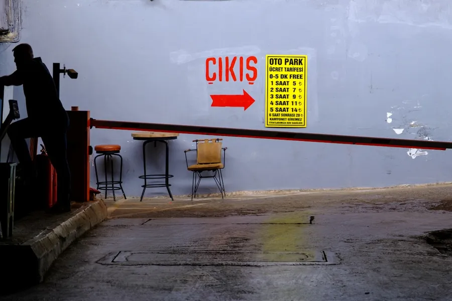 Ilustrasi mimpi tukang parkir — Silhouette of person near parking barrier with exit sign.