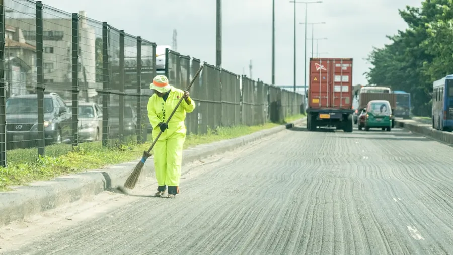 Ilustrasi mimpi tukang sapu — man in green jacket and green pants holding shovel walking on road during daytime